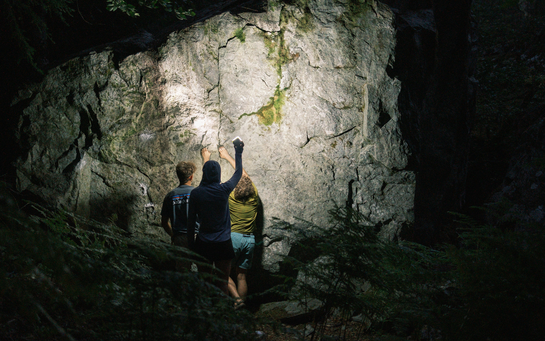 Climbers stand before a route lit by headlamp